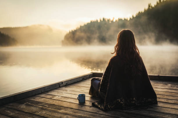 Woman relaxing with a cup of coffee in the nature stock photo. Woman drinking coffee near a lake in the morning.